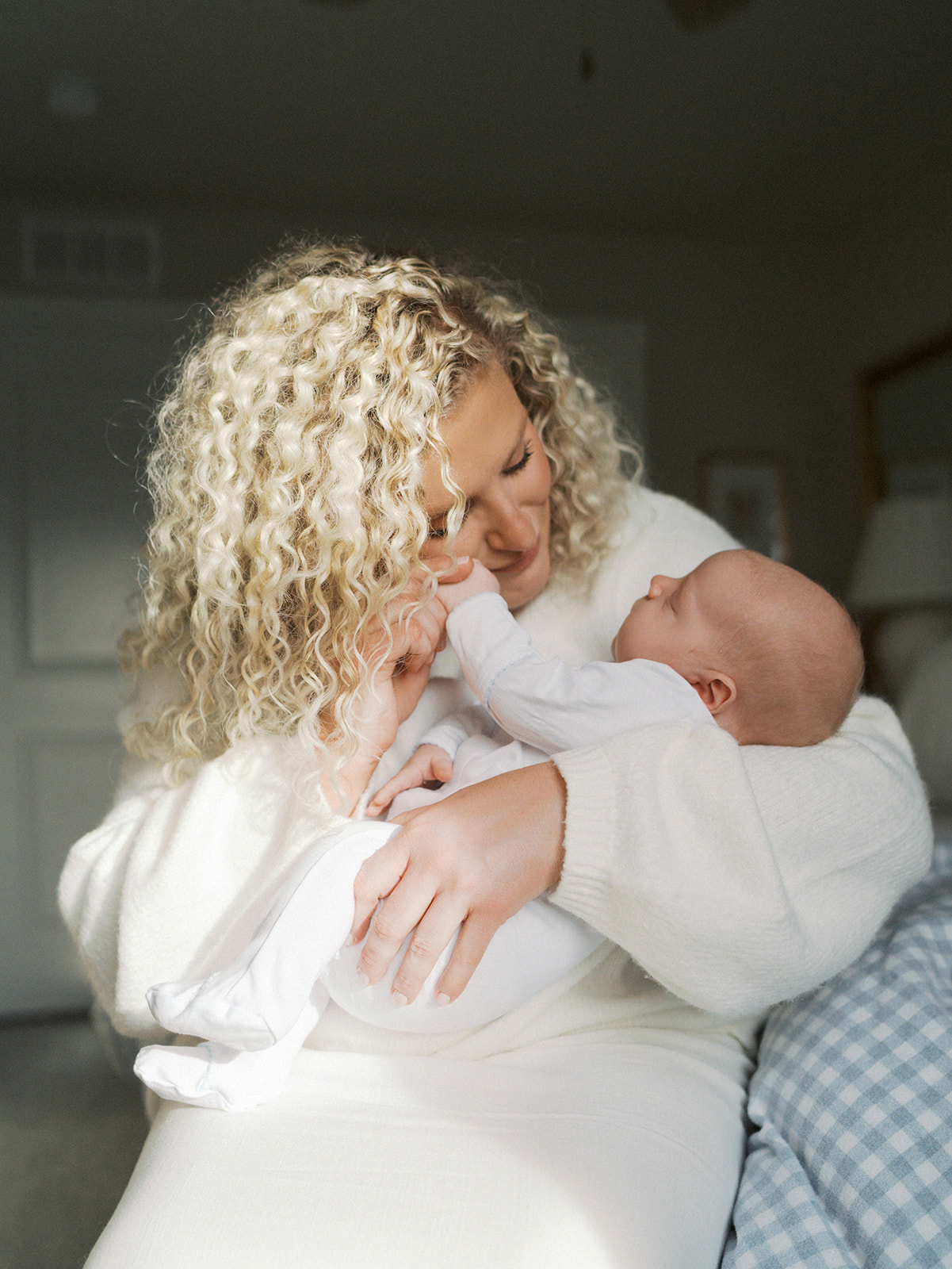a mother looks lovingly at her newborn son while she holds his tiny hand against her cheek